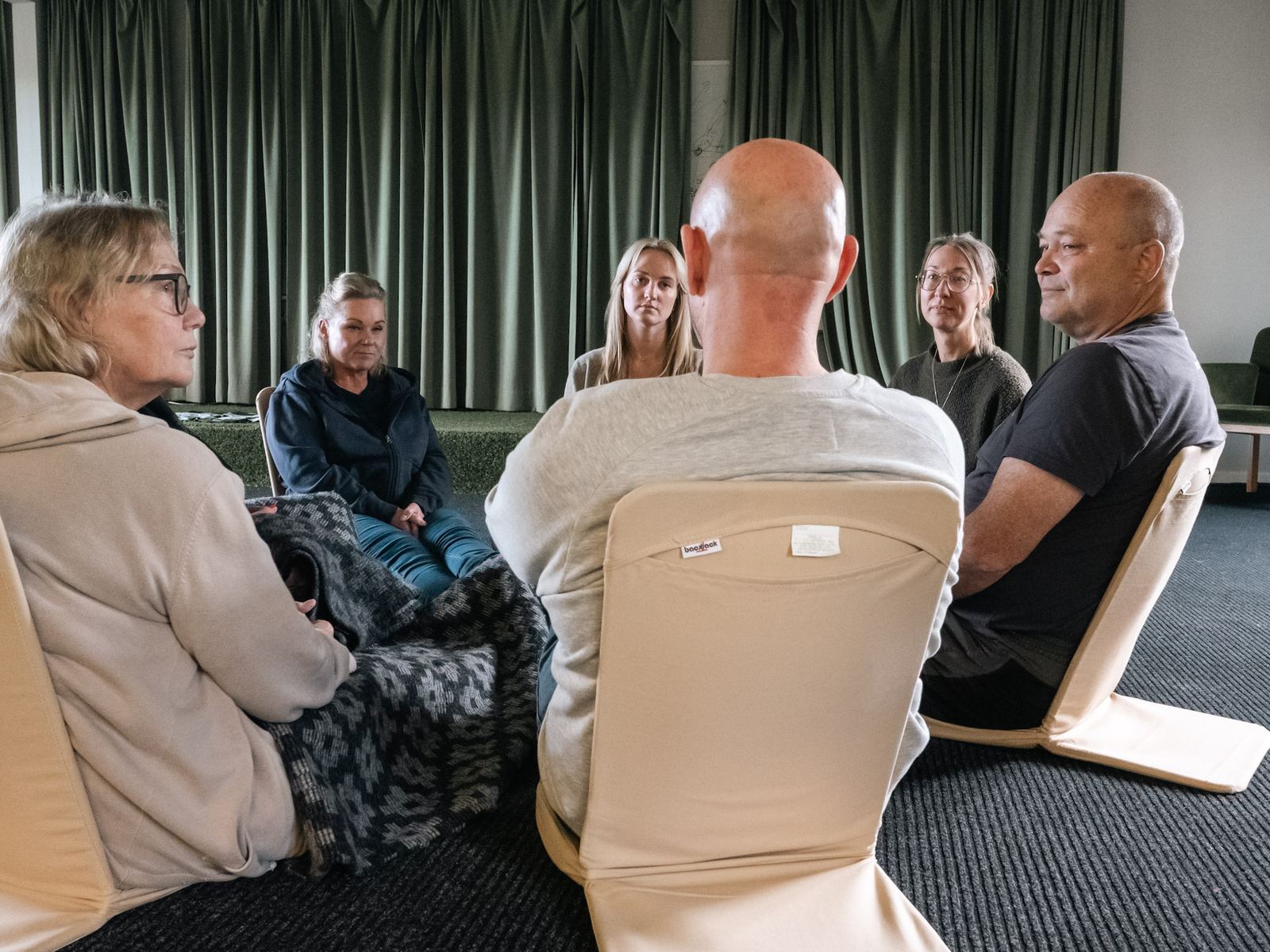 Deltagare sitter på golvstolar i salen, vända mot varandra.