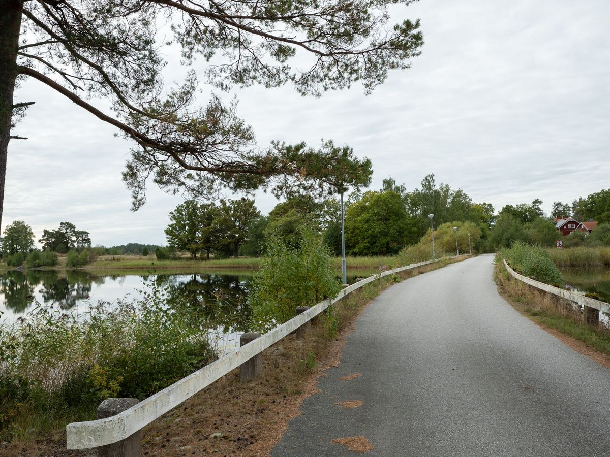 Vägen över vattnet, med träd och ett rött hus i bortre änden.