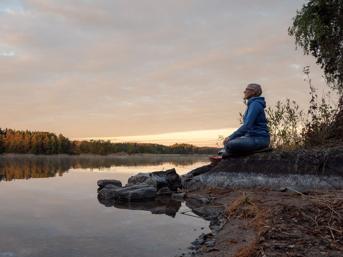 En person sitter stilla på en sten vid sjön i morgonljuset.