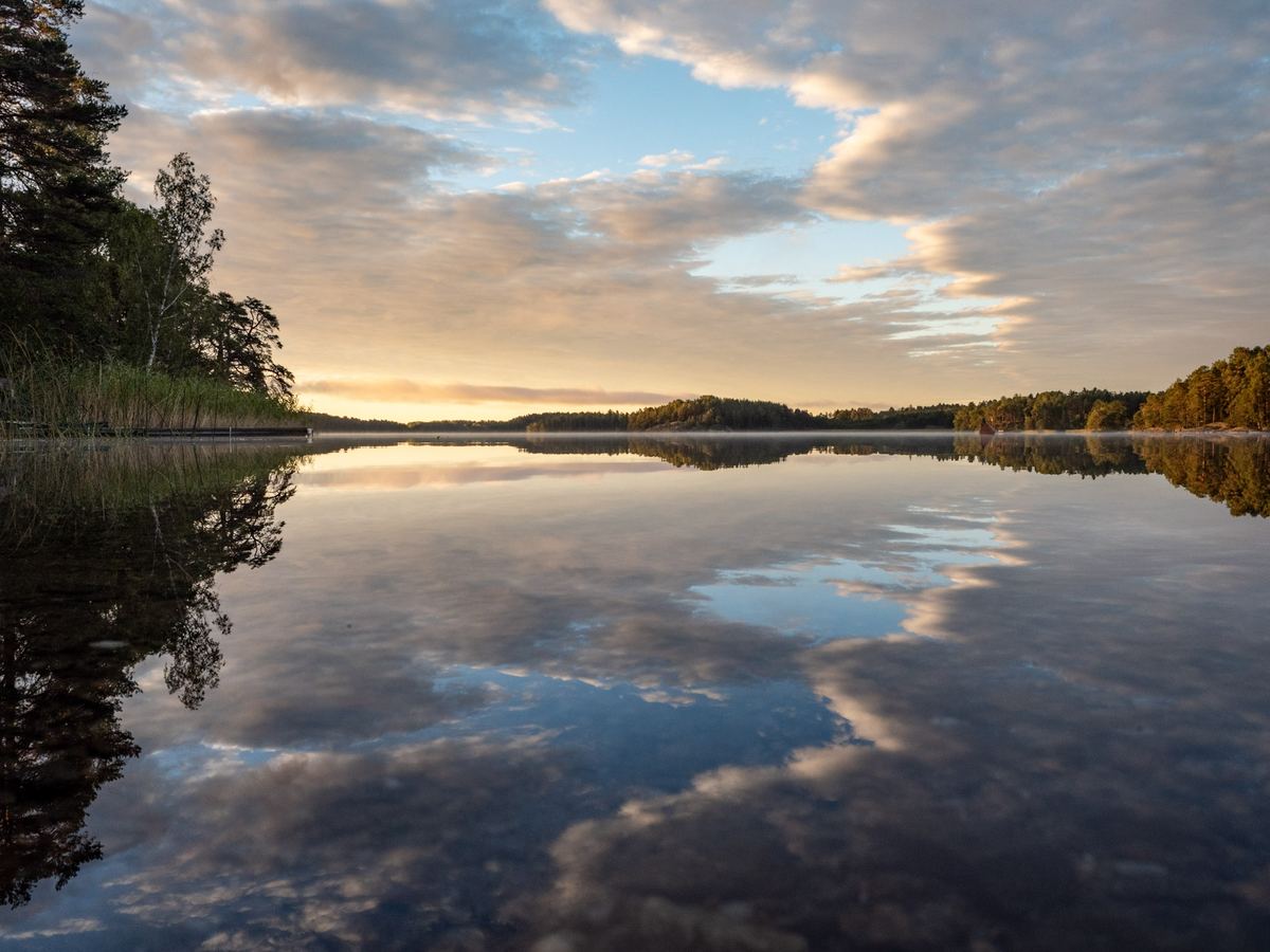 Spegelblank sjö med moln som speglas i vattnet.